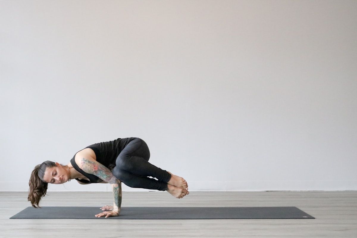 Woman in black tank top and gray leggings in an advanced yoga pose